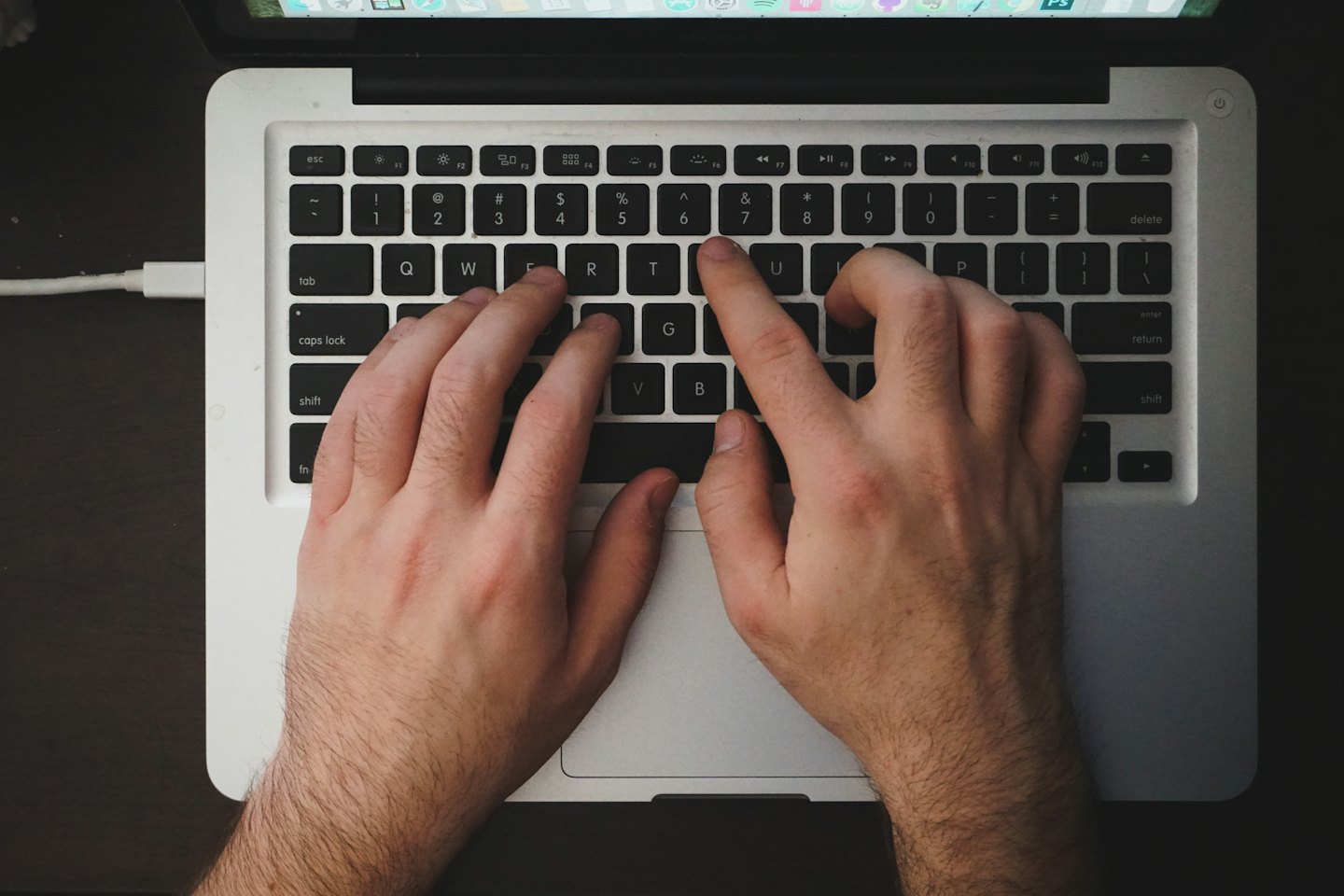 Manos escribiendo en el teclado de un portátil con la pantalla visible.